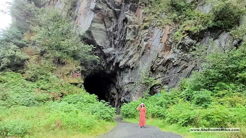 A Woman Standing In Front Of A Cave With Old Railroad Tunnel In The Background